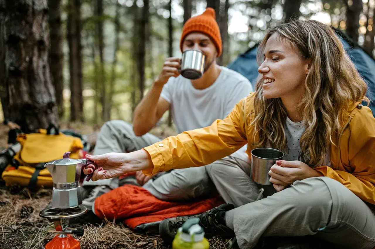 Ein Paar genießt Kaffee aus Metallbechern im Wald. Tolle Mikroabenteuer Ideen für eine Auszeit in der Natur.