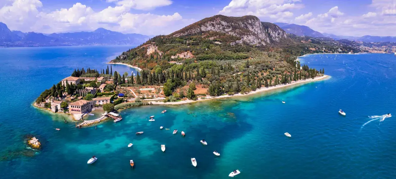 Punta San Vigilio: malerische Halbinsel mit historischen Gebäuden, Olivenhainen und dem türkisfarbenen Gardasee, belebt durch zahlreiche Boote.