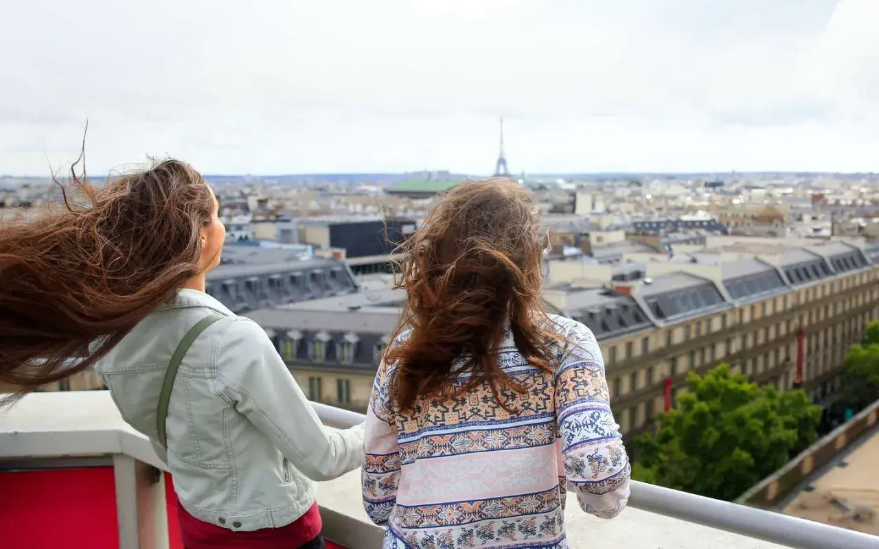 Zwei Teenager genießen den Blick über Paris. Der Wind spielt mit ihren Haaren, während sie die Stadt und den Eiffelturm bestaunen.