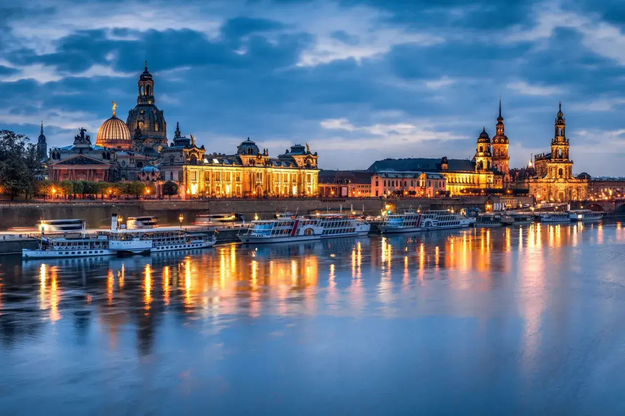Dresden bei Nacht: beleuchtete Frauenkirche und Zwinger spiegeln sich im Wasser. Perfekte Reiseziele im November in Deutschland.