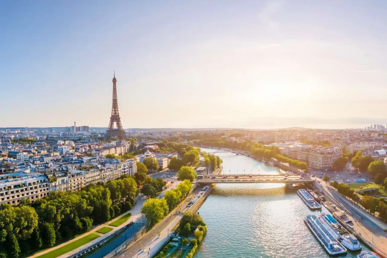 Paris im Sommer: Eiffelturm ragt über die Stadt, die Seine fließt friedlich, Boote liegen am Ufer. Ein malerischer Ausblick.