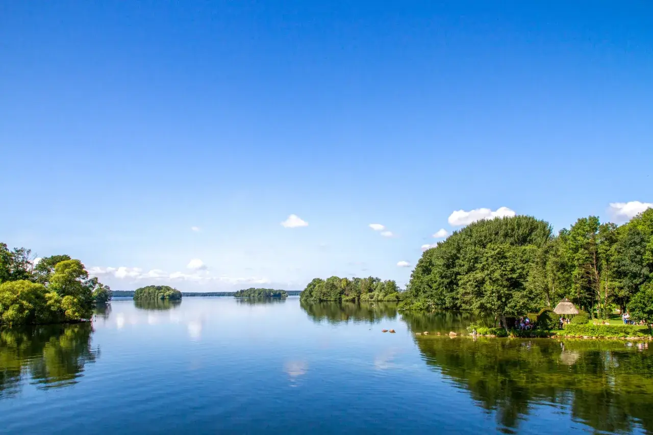 Idyllische Seenlandschaft in Norddeutschland mit grünen Ufern, Inseln und einem klaren blauen Himmel.