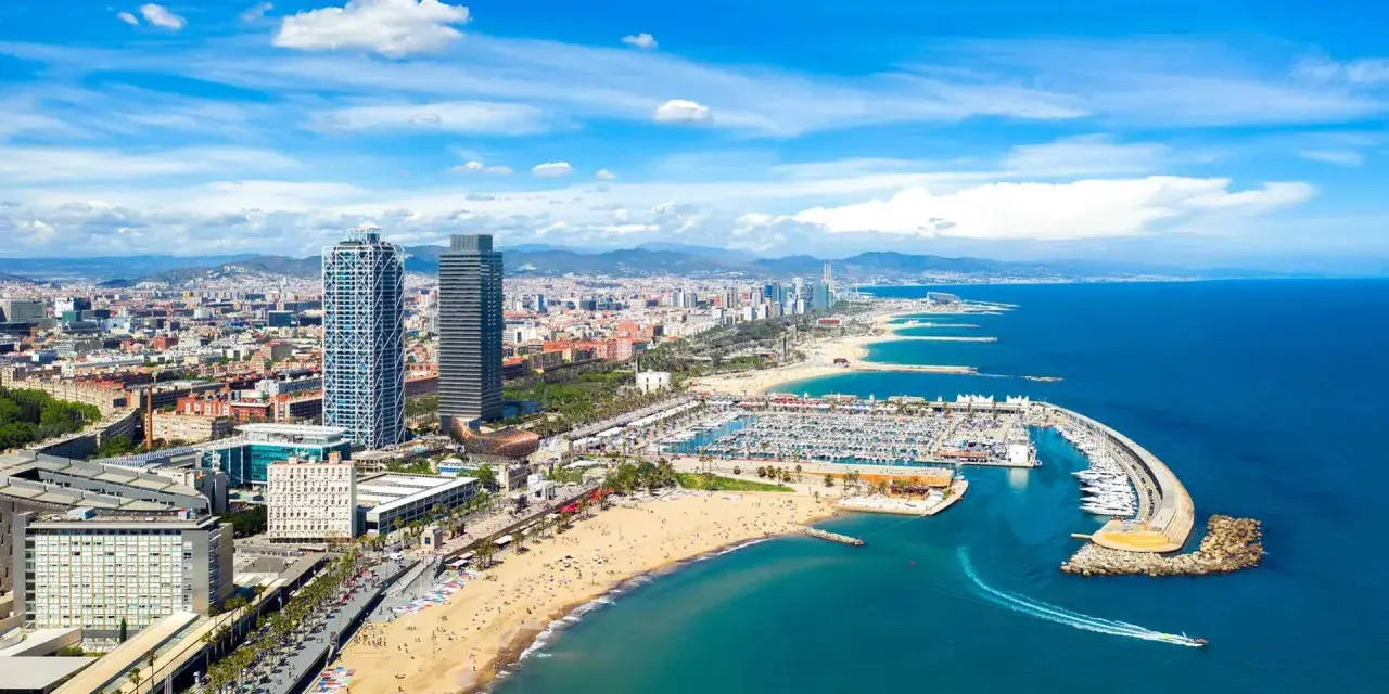 Blick auf den belebten barcelona strand mit Yachten im Hafen und der Skyline der Stadt im Hintergrund.