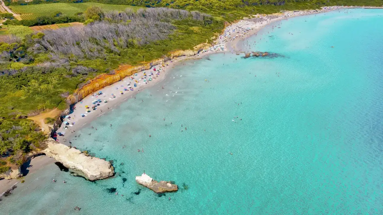 Traumhafter Strand in Apulien mit türkisfarbenem Wasser, sonnenhungrigen Menschen und grünen Hügeln im Hintergrund.