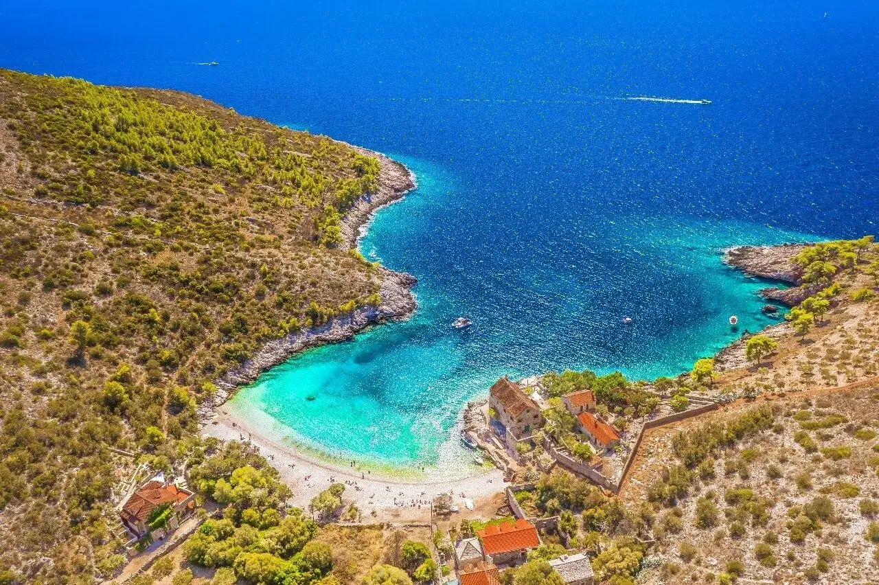 Traumhafter istrien strand mit türkisfarbenem Wasser, weißen Kieselsteinen und alten Steinhäusern.