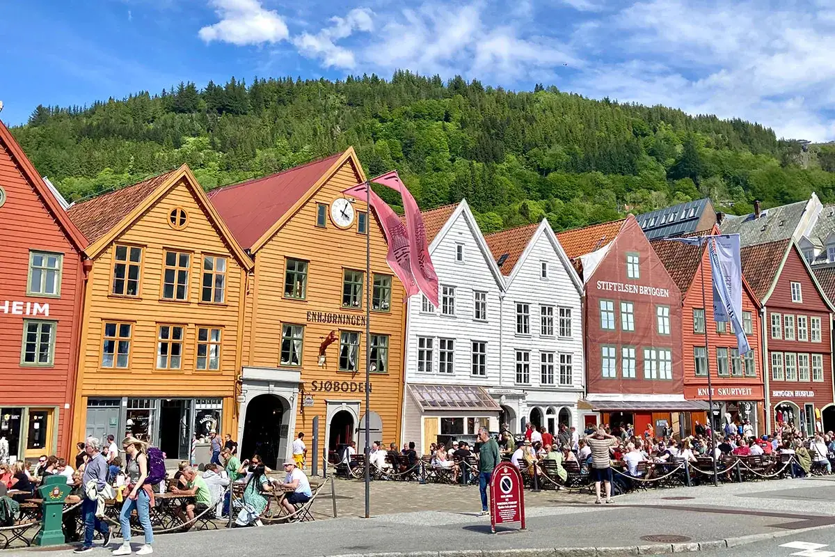 Bunte Holzhäuser am Wasser in der Bergen Altstadt, mit vielen Menschen, die draußen sitzen.