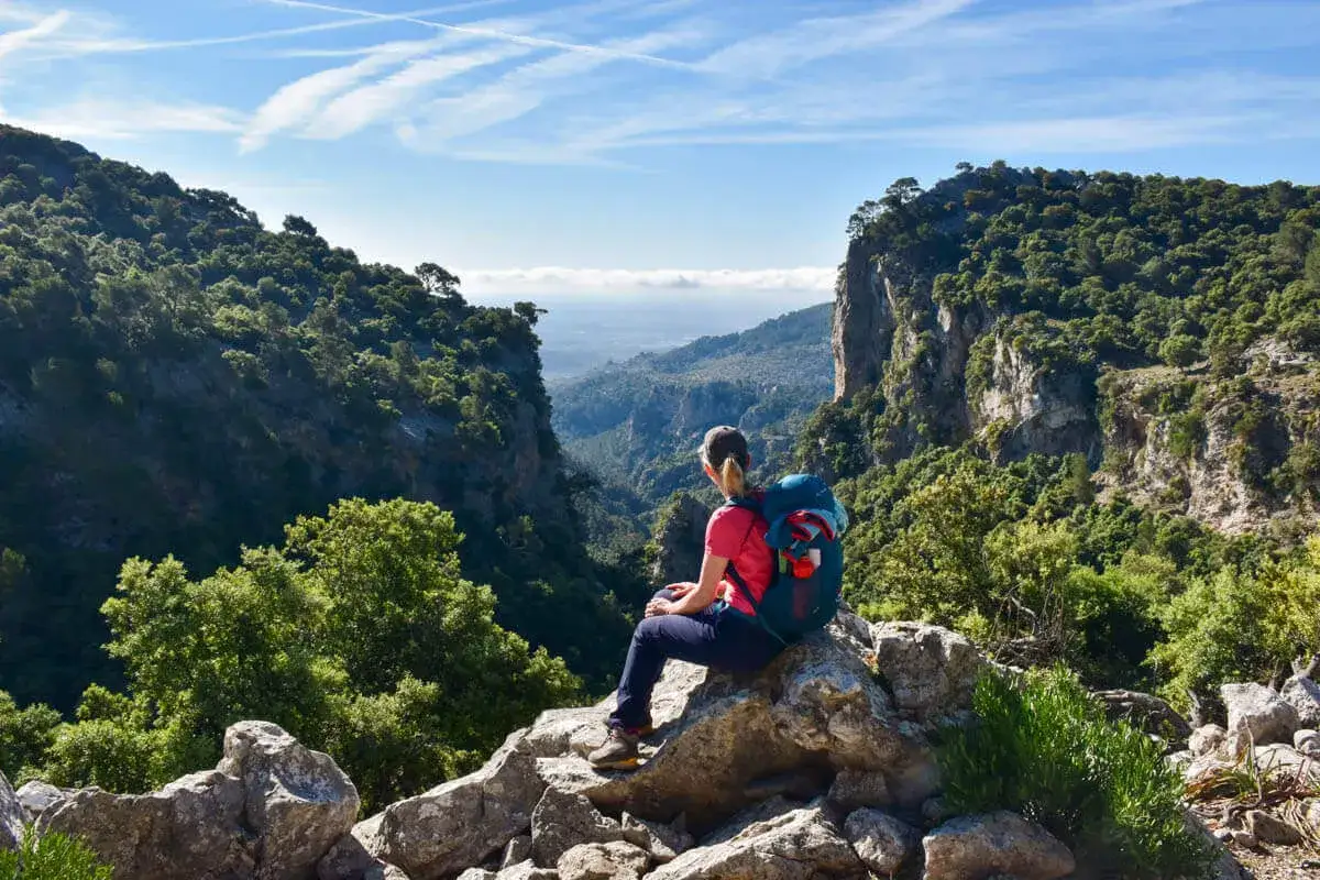 Wanderer mit Rucksack auf Felsen sitzend, genie&szlig;t die Aussicht auf ein tiefes Tal auf dem Mallorca Fernwanderweg.