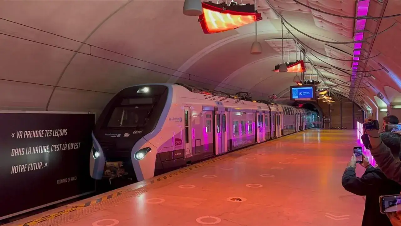 Moderner Zug im Bahnhof Saint-Lazare, beleuchtet in Pink. Eine Tafel zitiert Leonardo da Vinci.
