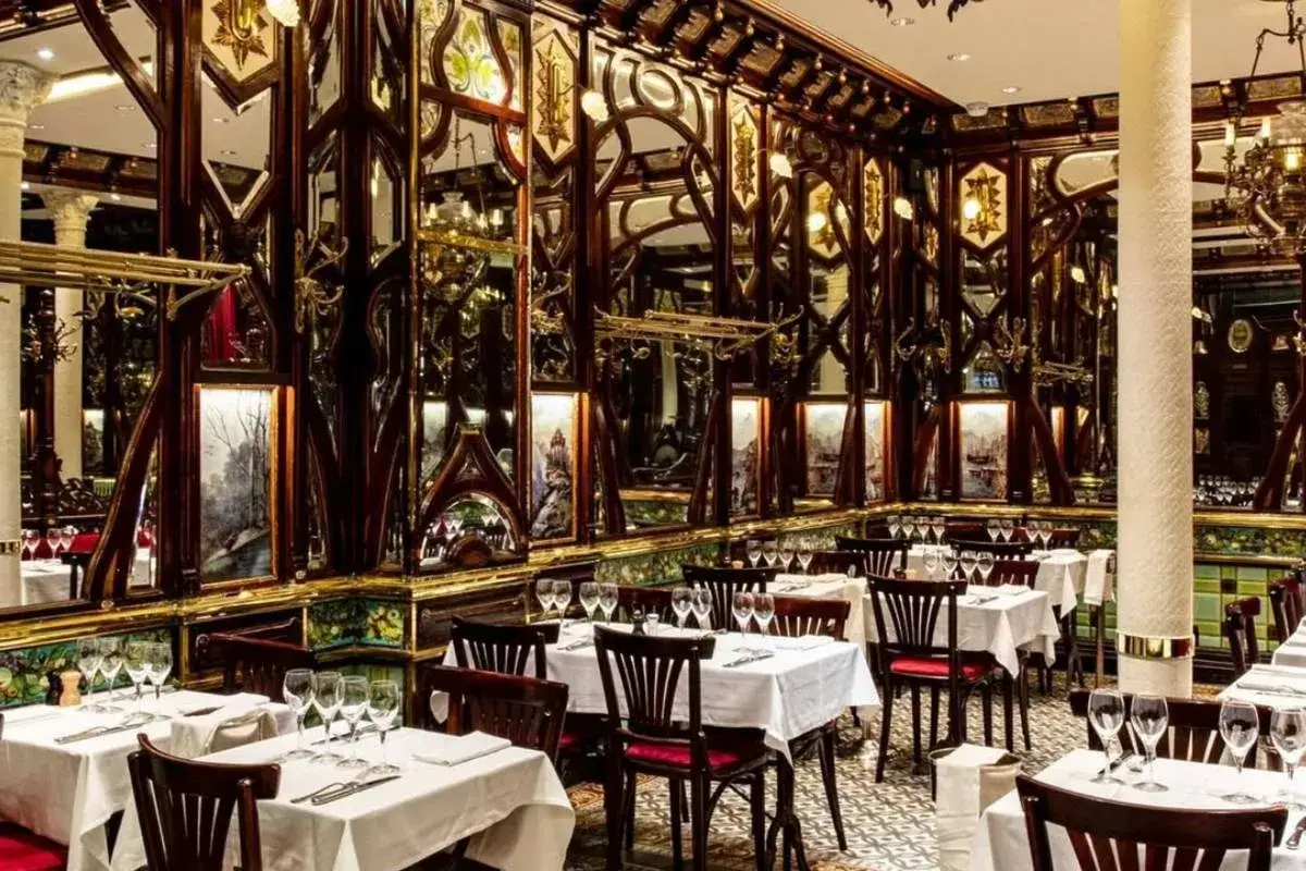Prunkvoller Speisesaal im La Coupole Paris, mit Spiegeln, Holzschnitzereien und gedeckten Tischen.