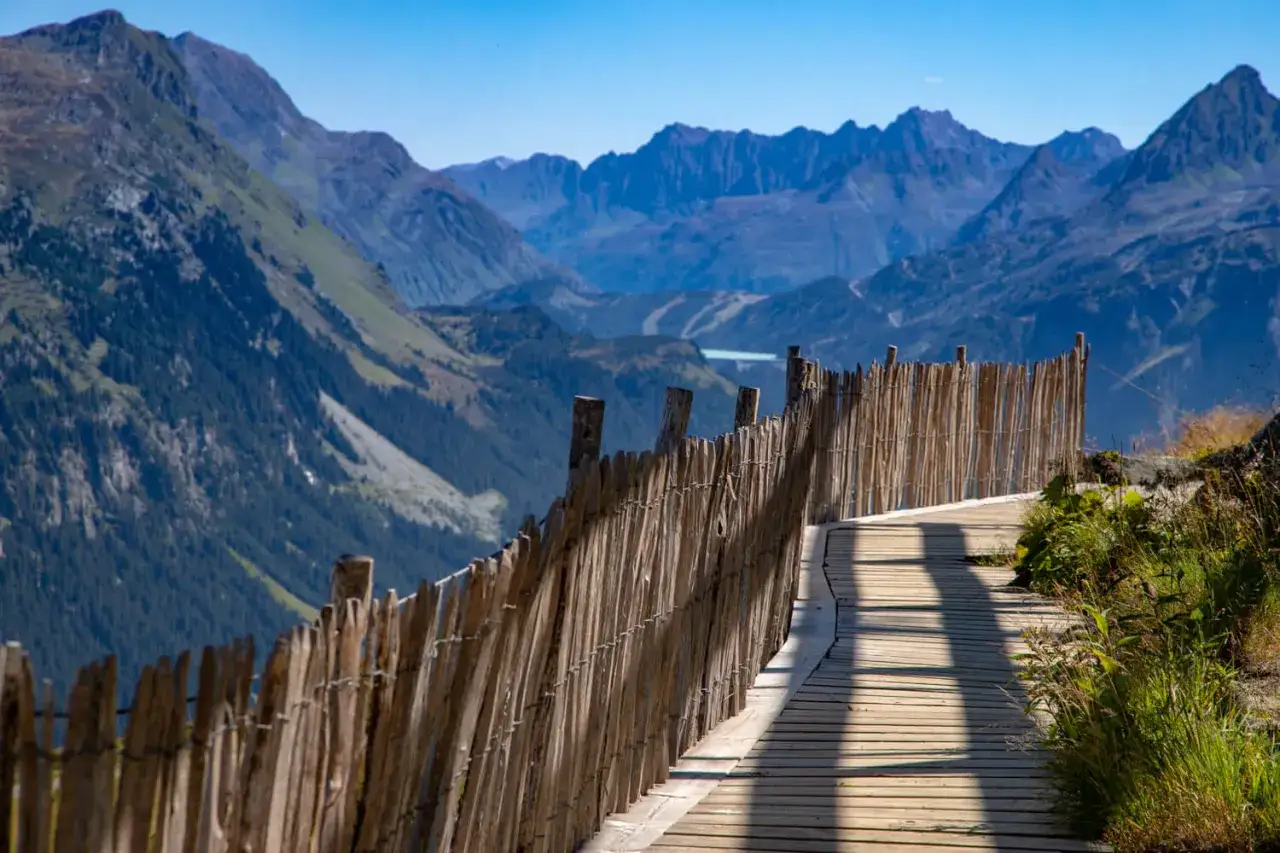 Holzsteg mit rustikalem Zaun f&uuml;hrt durch die Berglandschaft des Montafon. Perfekt f&uuml;r Wanderungen.