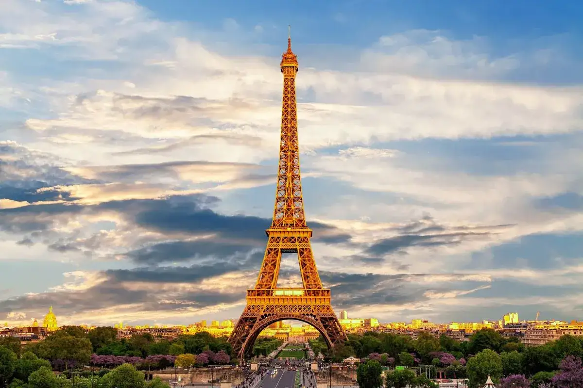 Eiffelturm im Abendlicht, ein absolutes Paris must see. Die Stadt erstrahlt, während Wolken den Himmel zieren.