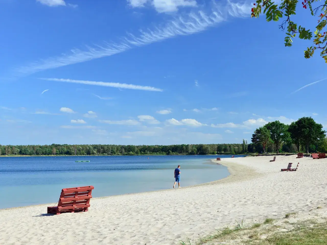 Ein Mann spaziert am Strand eines Sees in Norddeutschland. Rote Liegestühle stehen bereit.