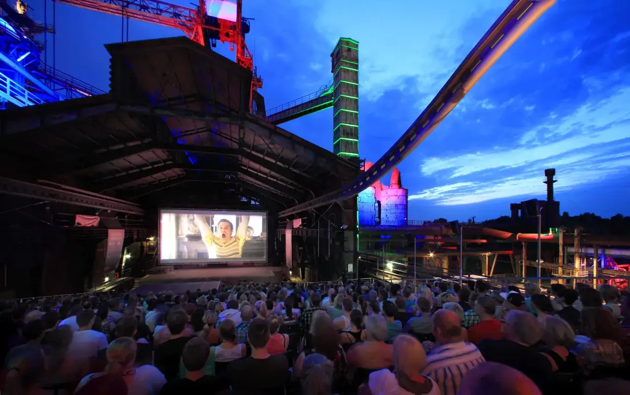 Open-Air-Kino in NRW: Menschen genießen einen Film vor beeindruckender Industriekulisse bei Nacht.