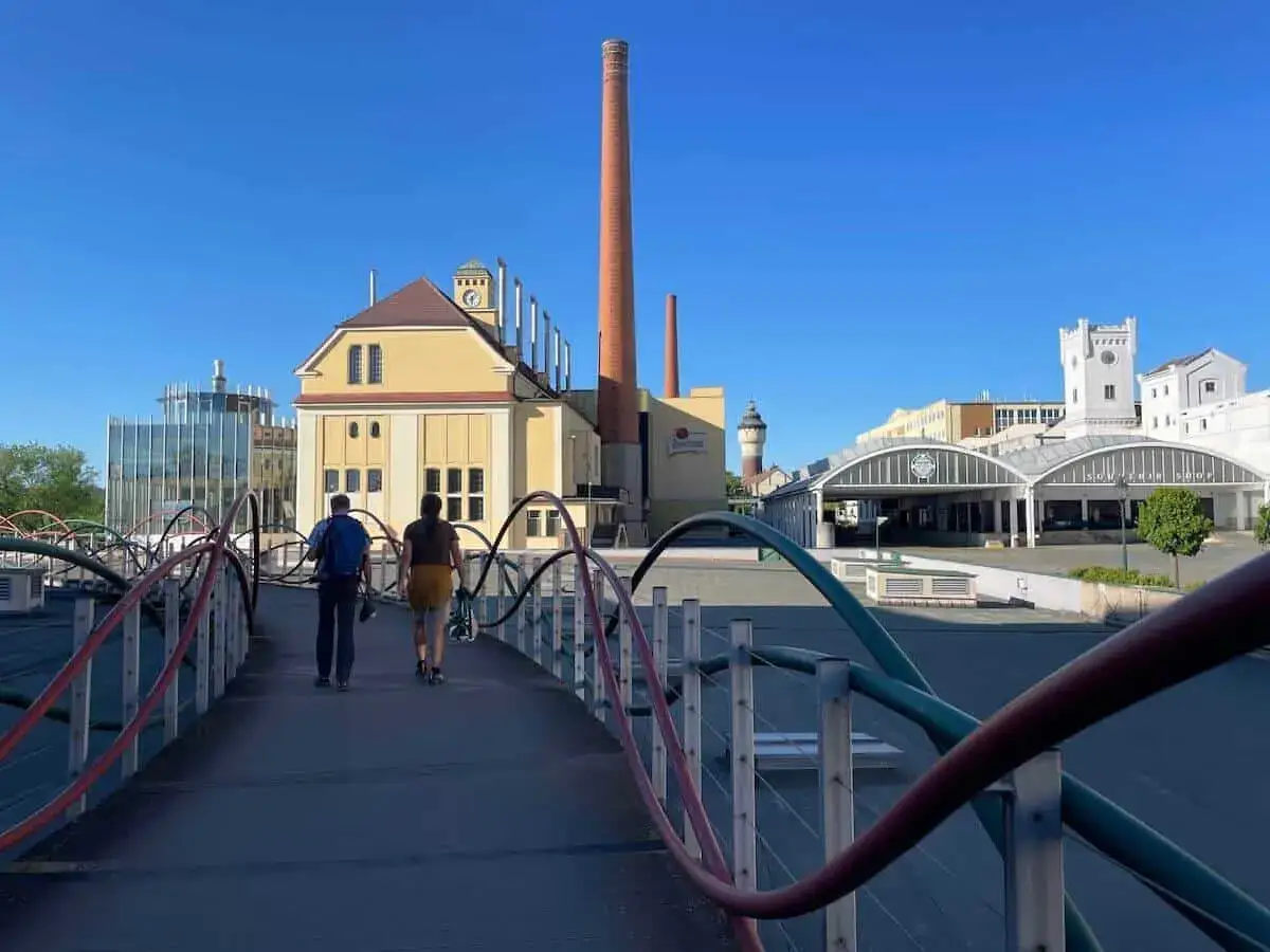 Zwei Personen &uuml;berqueren eine Br&uuml;cke mit Blick auf die Pilsner Brauerei. Ein perfekter Ort f&uuml;r Pilsen Geheimtipps abseits der Touristenpfade.