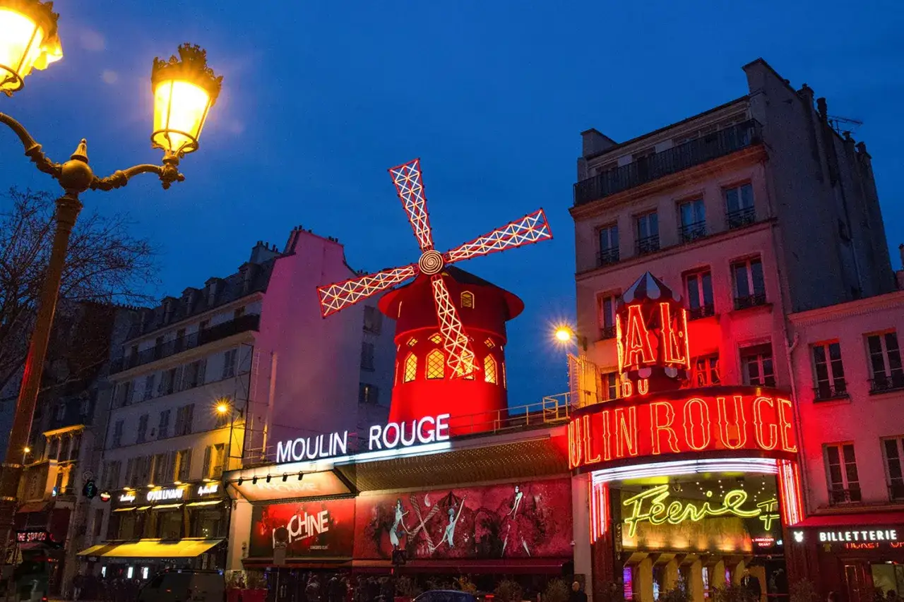 Das Moulin Rouge in Paris bei Nacht, mit seinem ikonischen roten Windrad und leuchtenden Neonschildern, die die Frage 