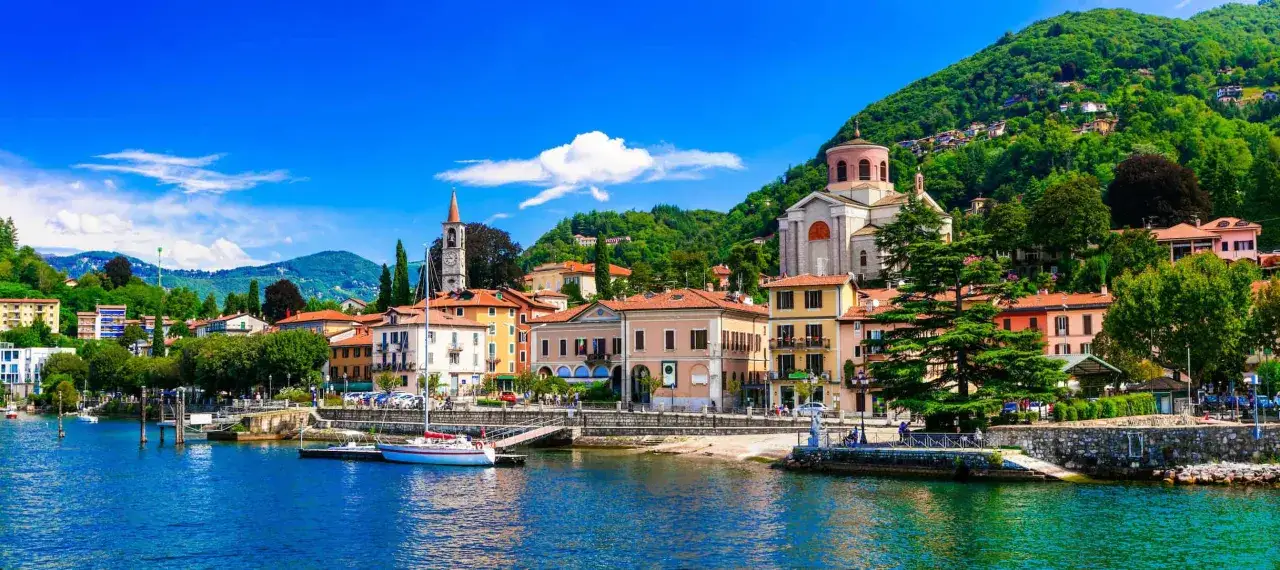 Bunte Häuser am Lago Maggiore, ein Kirchturm und grüne Hügel. Hier sind die besten Lago Maggiore Insider Tipps für Ihren Urlaub.