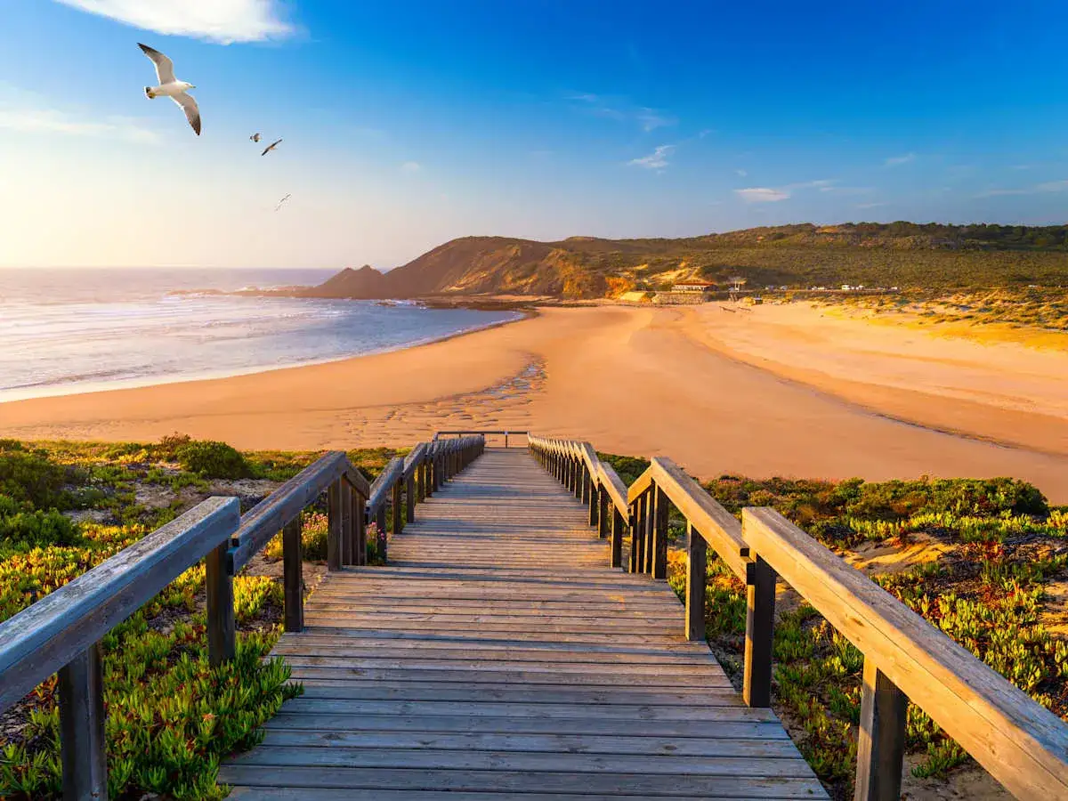 Holzsteg f&uuml;hrt zu einem einsamen Strand an der Algarve. M&ouml;wen kreisen &uuml;ber dem Meer. Ein perfekter Ort f&uuml;r Algarve Geheimtipps.