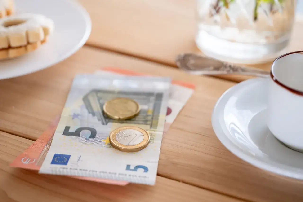 Euro-Scheine und M&uuml;nzen liegen auf einem Holztisch, bereit als trinkgeld paris. Daneben eine Kaffeetasse und Kekse.