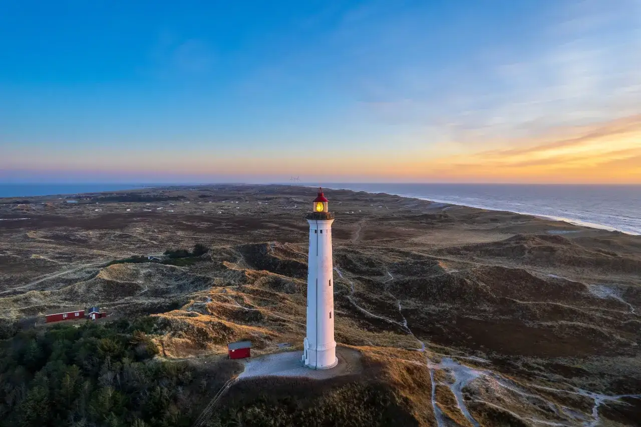 Leuchtturm bei Sonnenuntergang an der Küste, umgeben von Dünen. Ein versteckter Ort, der an Hvide Sande Geheimtipps erinnert.