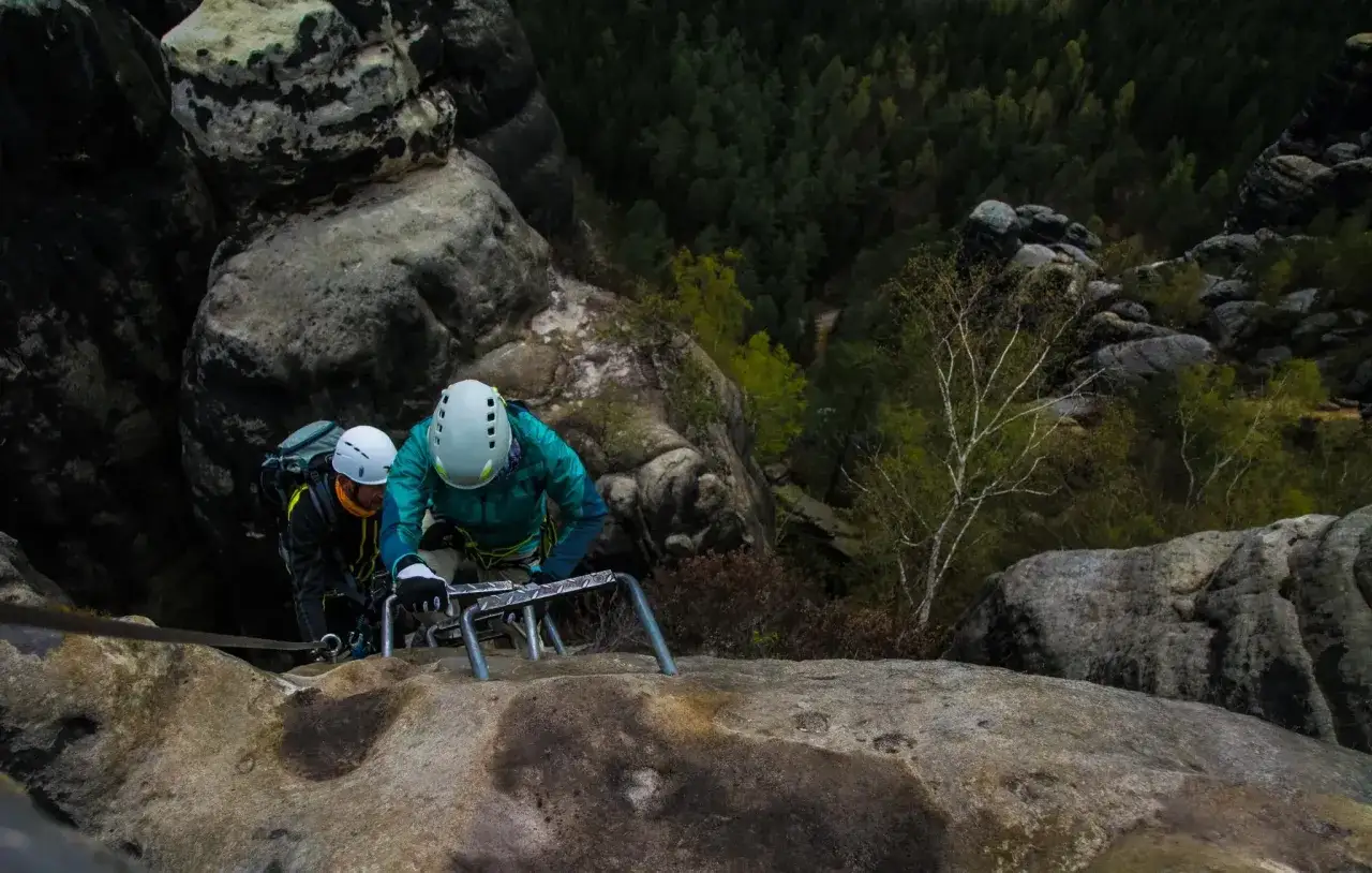 Zwei Kletterer meistern einen anspruchsvollen Klettersteig im Elbsandsteingebirge. Sie sichern sich an Stahlseilen und Tritten, w&auml;hrend sie die Felsen erklimmen.