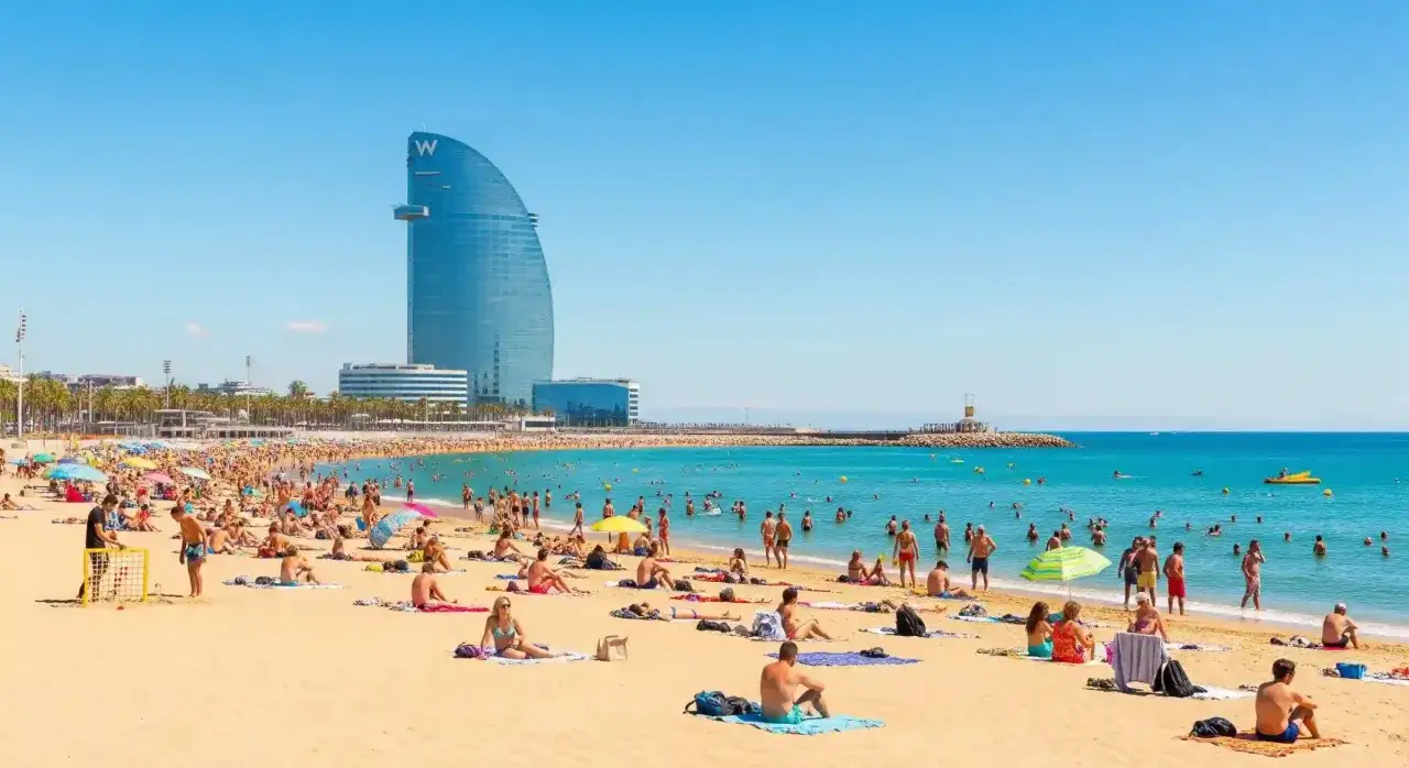 Sonniger barcelona strand mit vielen Menschen, die sich sonnen und im Meer schwimmen. Im Hintergrund das markante W Hotel.