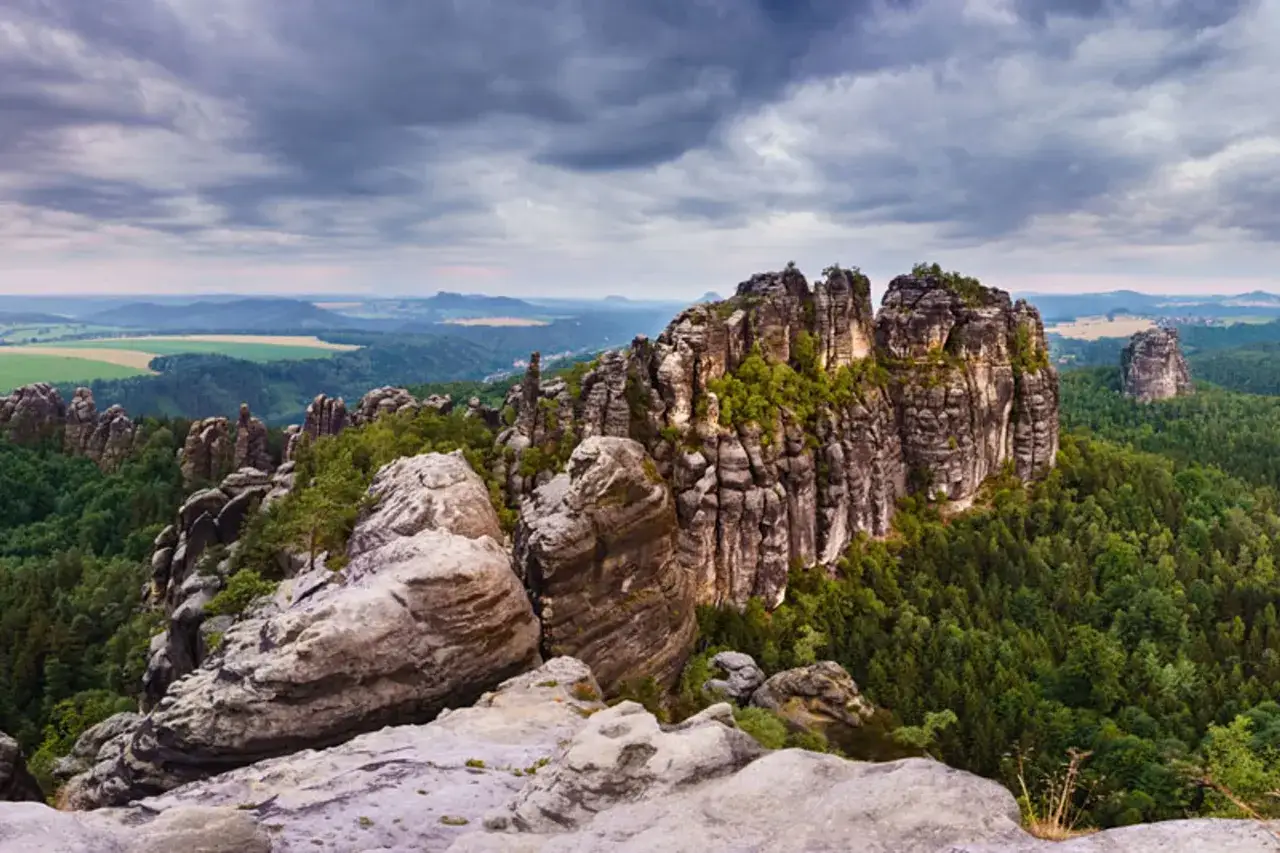 Blick &uuml;ber die Schrammsteine bei einer leichten Wanderung. Felsformationen ragen aus einem dichten Nadelwald empor, im Hintergrund sanfte H&uuml;gel.