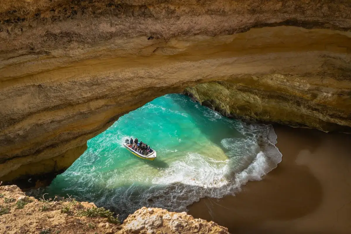Boot erkundet versteckte Höhle am Strand Algarve Geheimtipp. Türkises Wasser, Felsen und Sand.