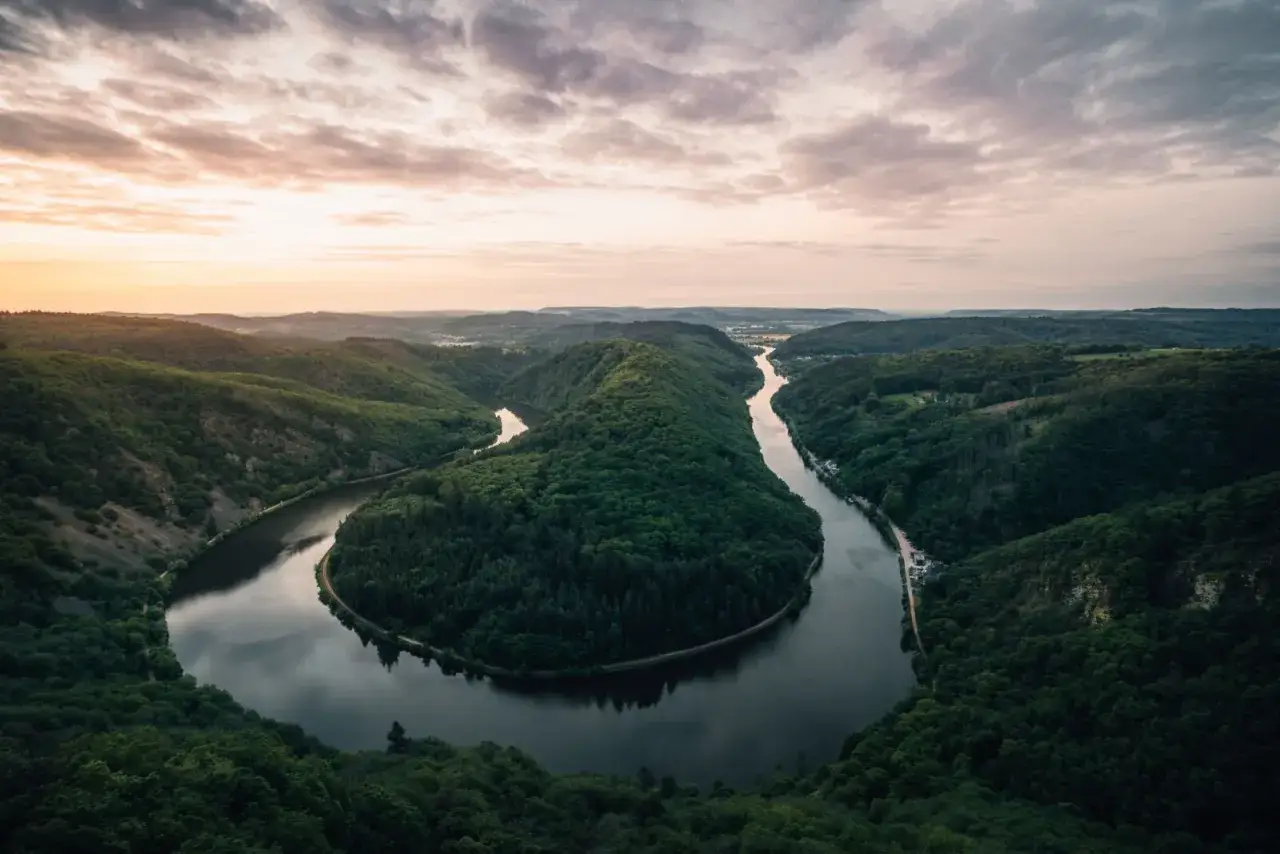 Eine Flussbiegung im Saarland, die an eine Traumschleife erinnert. Grüne Hügel und ein ruhiger Fluss unter einem dramatischen Himmel.