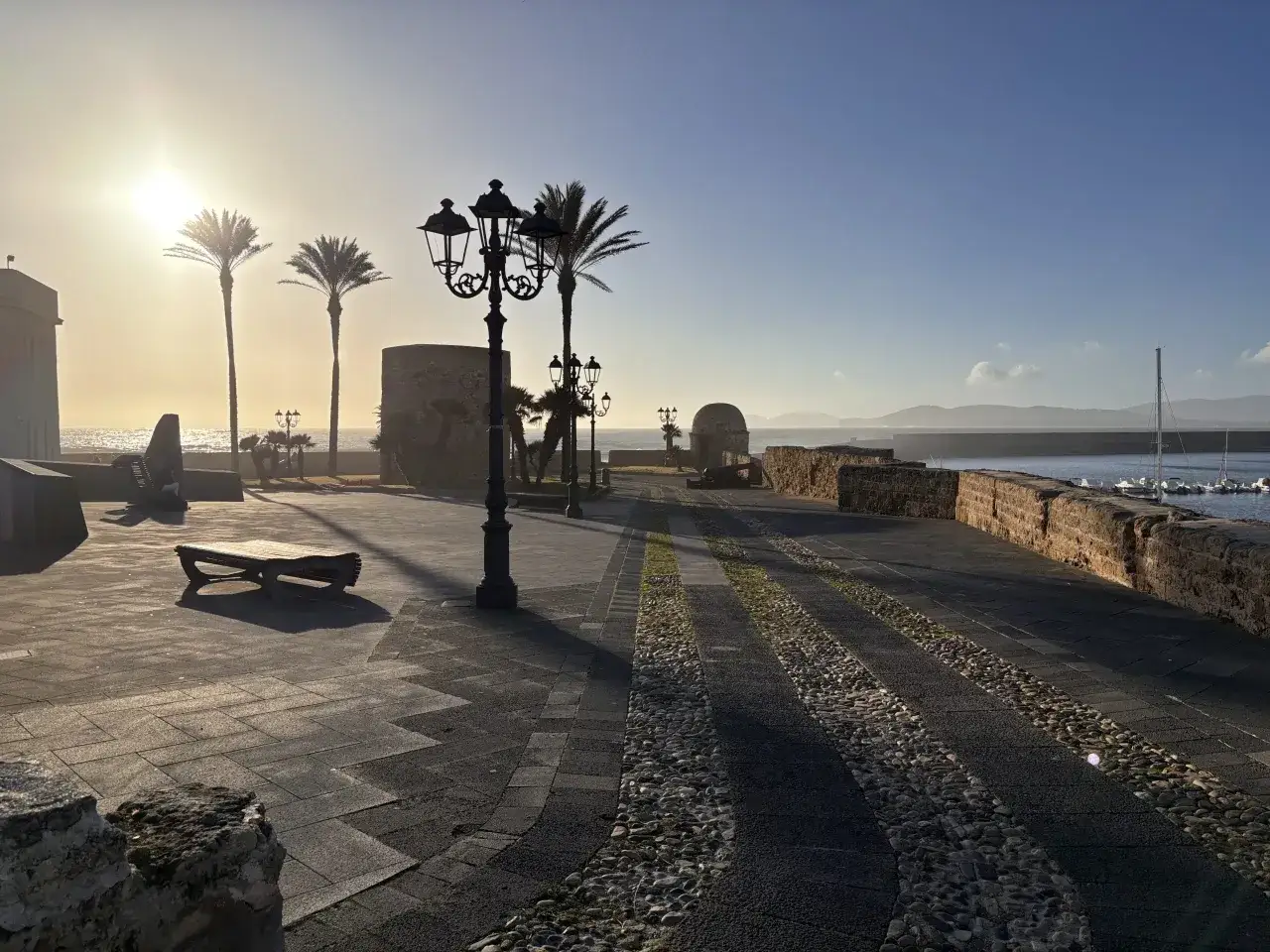 Sonnenuntergang an der Promenade der alghero altstadt. Palmen, Laternen und das Meer im warmen Licht.