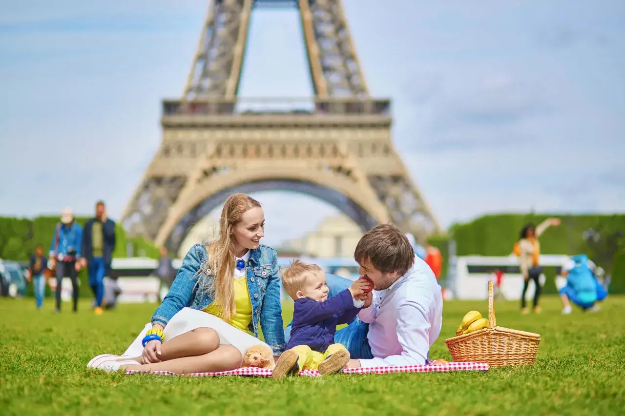 Familie genie&szlig;t ein Picknick in einem der Parks in Paris mit dem Eiffelturm im Hintergrund.