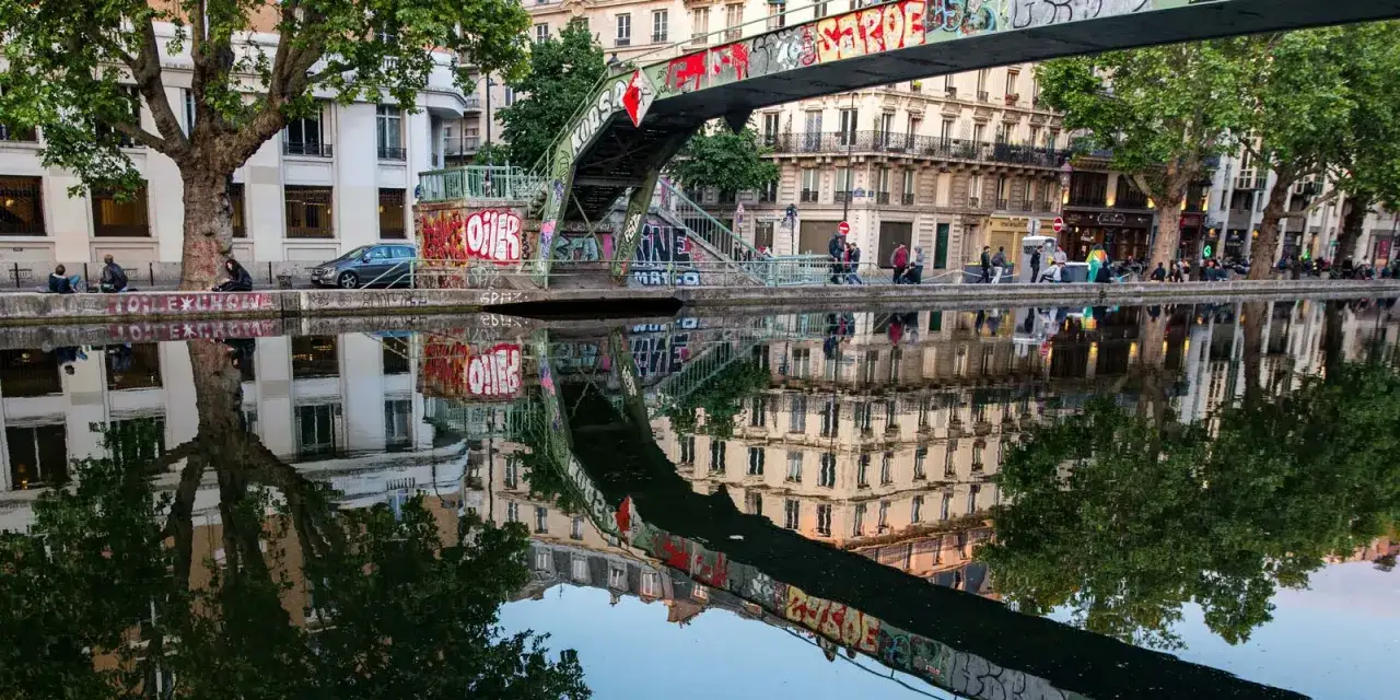 Ein malerischer Kanal in Paris, mit reflektierenden Gebäuden und Bäumen. Man kann sich vorstellen, wie schön es wäre, hier Fahrrad zu fahren in Paris.