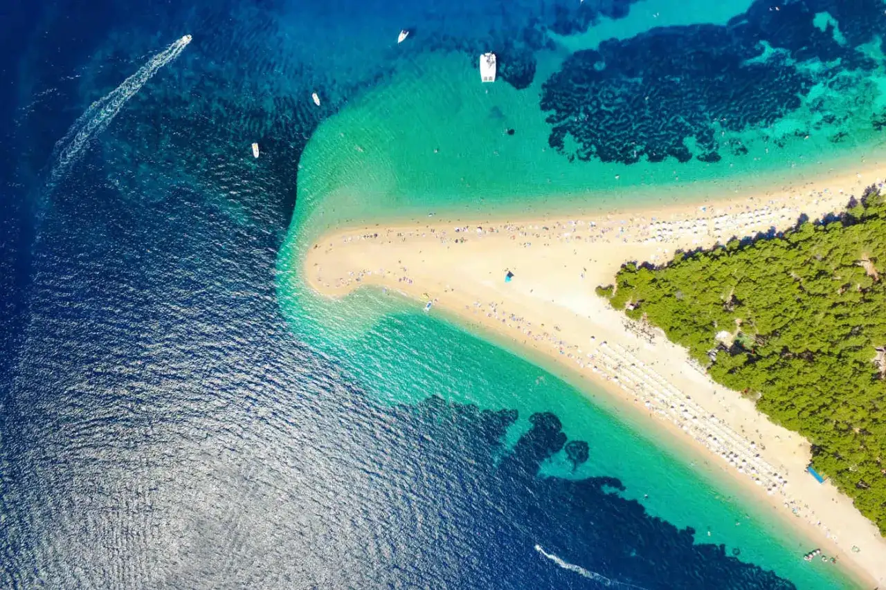 Traumhafter Strand auf einer kroatischen Insel mit türkisfarbenem Wasser, Pinienwald und vielen Sonnenanbetern.