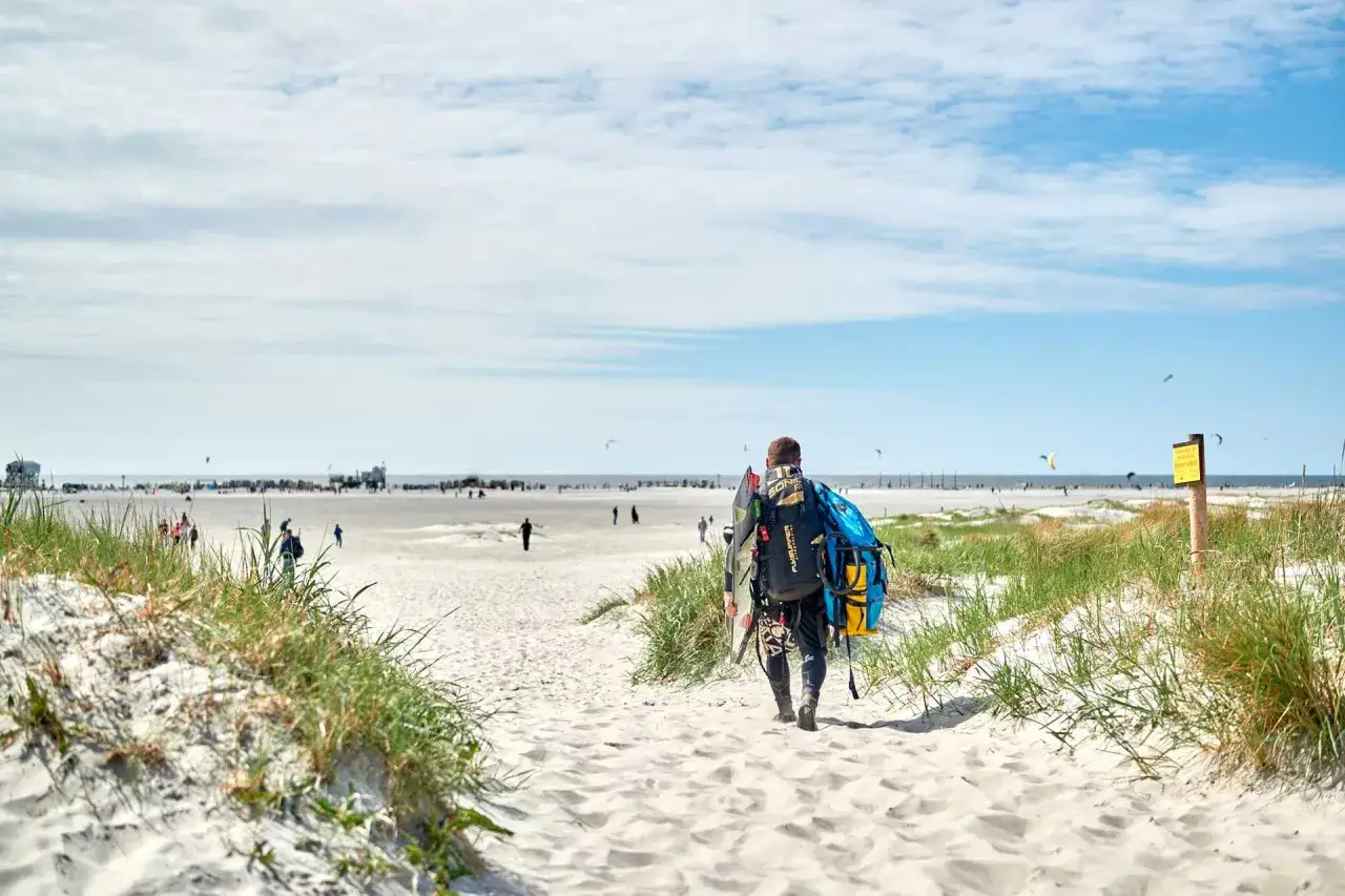 Kitesurfer mit Ausrüstung auf dem Weg zum Strand in St. Peter-Ording an der Nordsee.