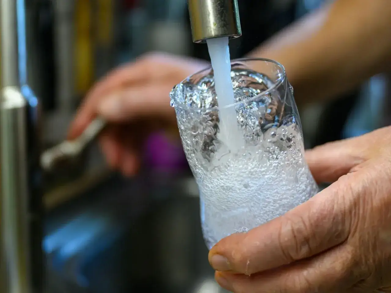 Hände füllen ein Glas mit sprudelndem Leitungswasser in Budapest.