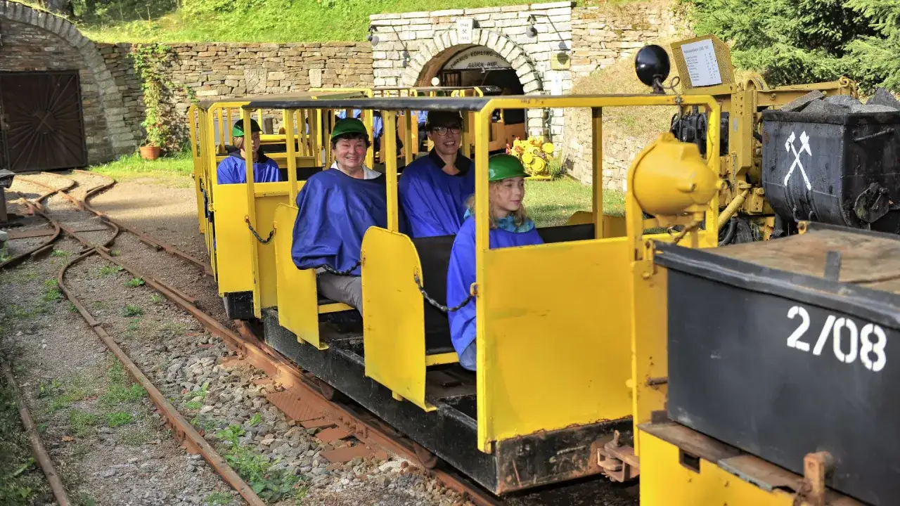 Besucher im Bergwerk Annaberg fahren in einem gelben Grubenbahnwaggon durch den Stollen.