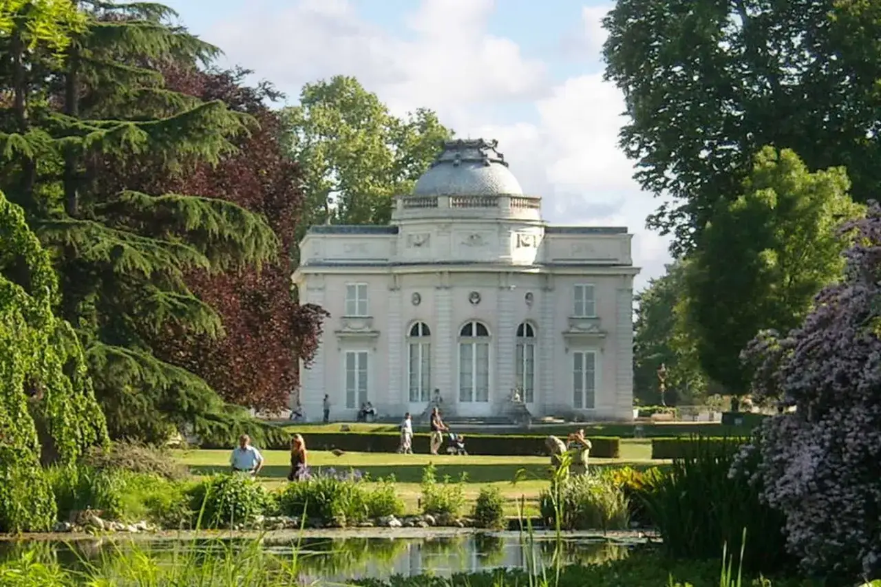 Ein sonniger Tag in Paris im Mai. Ein elegantes Gebäude mit Kuppel, umgeben von üppigem Grün und einem Teich. Menschen genießen den Park.