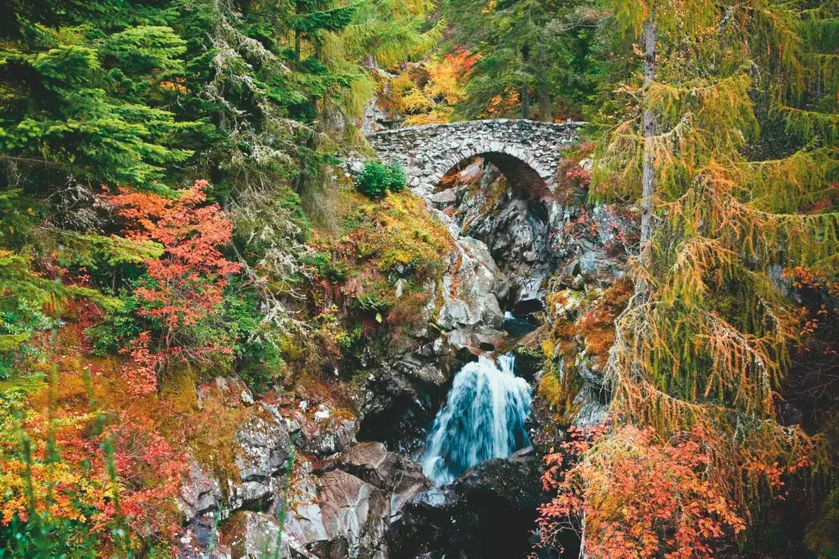 Herbstliche Farben im Cairngorms National Park beim Wandern. Ein Steinbogen überspannt einen Wasserfall.
