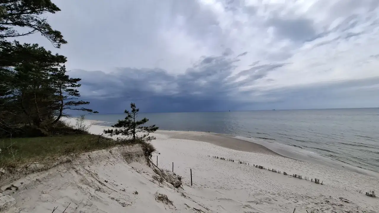 Einsamer Strand an der polnischen Ostsee, ein echter Geheimtipp. Dünen, Kiefern und das weite Meer unter dramatischem Himmel.