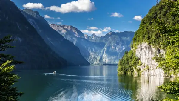 Ein Boot fährt auf einem ruhigen See, umgeben von steilen, bewaldeten Bergen. Ein idyllisches Bild von Badeseen Deutschland.