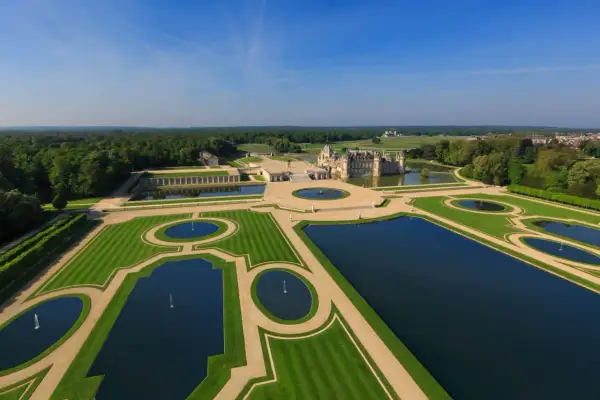 Das Chantilly Schloss mit seinen symmetrischen Wasserbecken und gepflegten Gärten, umgeben von einem weitläufigen Wald.