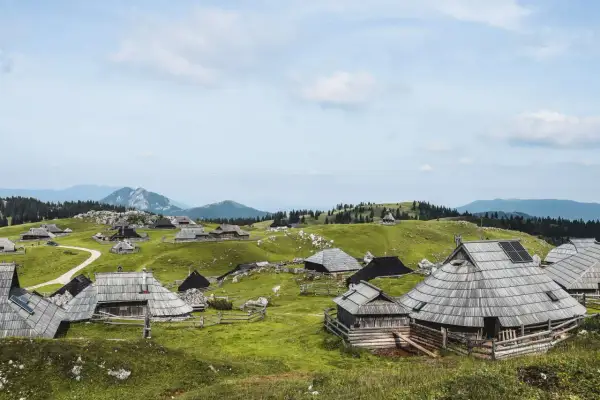 Idyllische Holzhütten auf grünen Hügeln, ein malerischer Ort für eine Velika Planina Wanderung. Berge im Hintergrund.