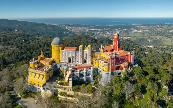 Buntes Schloss Pena thront auf Hügel, mit Blick auf das Meer. Ein grünes Auto parkt am sintra parking Weg.