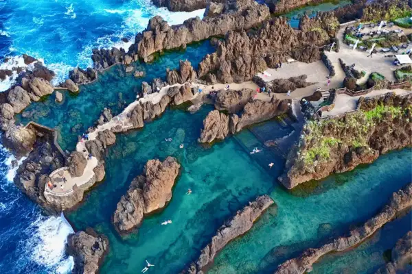 Natürliche Pools am **Strand Madeira**, umgeben von Felsen, mit klarem türkisfarbenem Wasser und badenden Menschen.