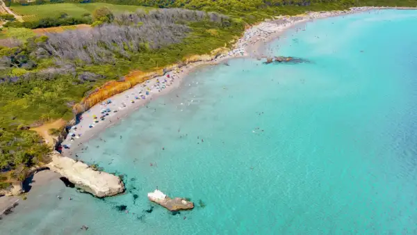 Traumhafter Strand in Apulien mit türkisfarbenem Wasser, sonnenhungrigen Menschen und grünen Hügeln im Hintergrund.