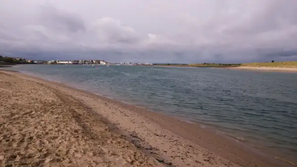 Sandiger Strand mit Blick auf eine Stadt und einen Yachthafen. Der Himmel ist bewölkt, aber das Wasser am Emden Strand ist ruhig.