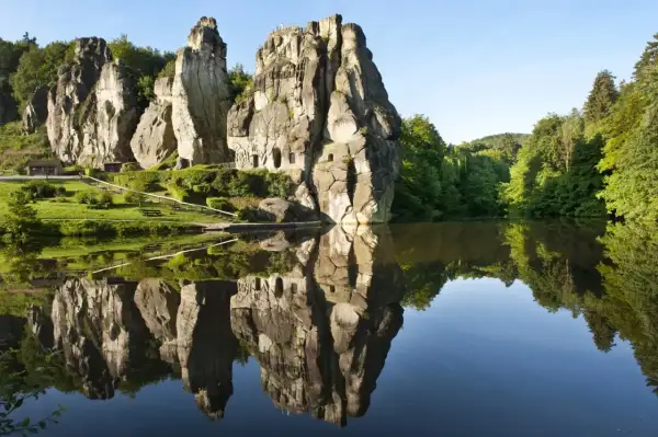 Felsformationen mit kleinen Höhlen spiegeln sich in einem ruhigen See. Ein idyllischer Ort für eine Wanderung im Teutoburger Wald.