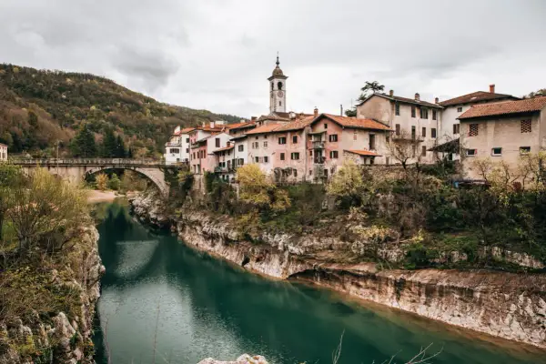 Idyllisches Dorf am Fluss Soča in Slowenien, mit einer Brücke und traditionellen Häusern, die sich an den Hang schmiegen.