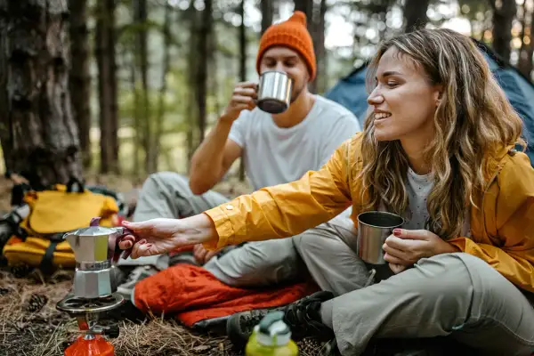 Ein Paar genießt Kaffee aus Metallbechern im Wald. Tolle Mikroabenteuer Ideen für eine Auszeit in der Natur.