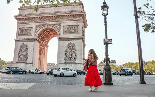 Frau in rotem Kleid tanzt vor dem Arc de Triomphe in Paris.