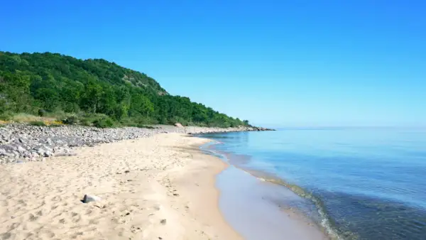 Sandstrand mit Felsen und grünen Hügeln, ein Highlight der schwedischen Landschaft.